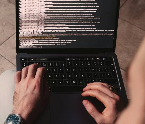 A close-up of a developer's hands coding on a laptop, with digital icons representing secure data